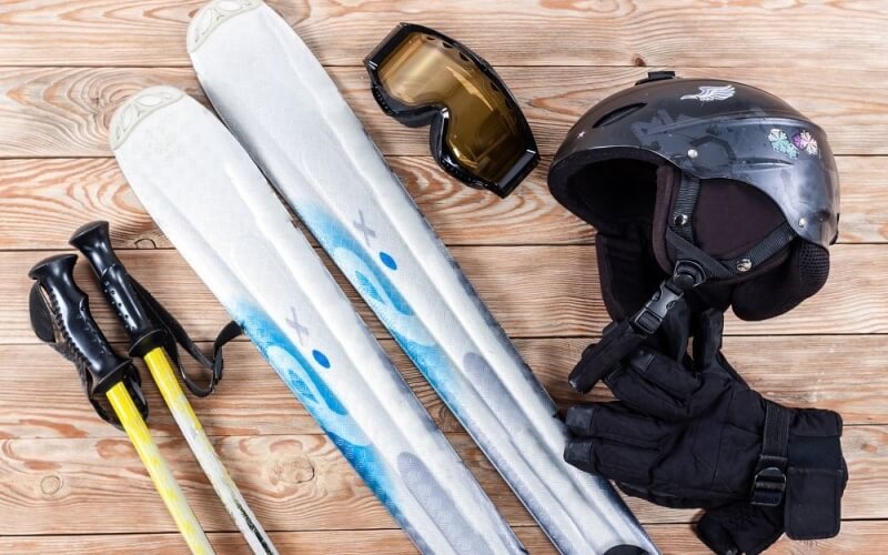 A collection of ski gear on a wooden surface, including skis, poles, a helmet, gloves, and goggles, arranged for display.