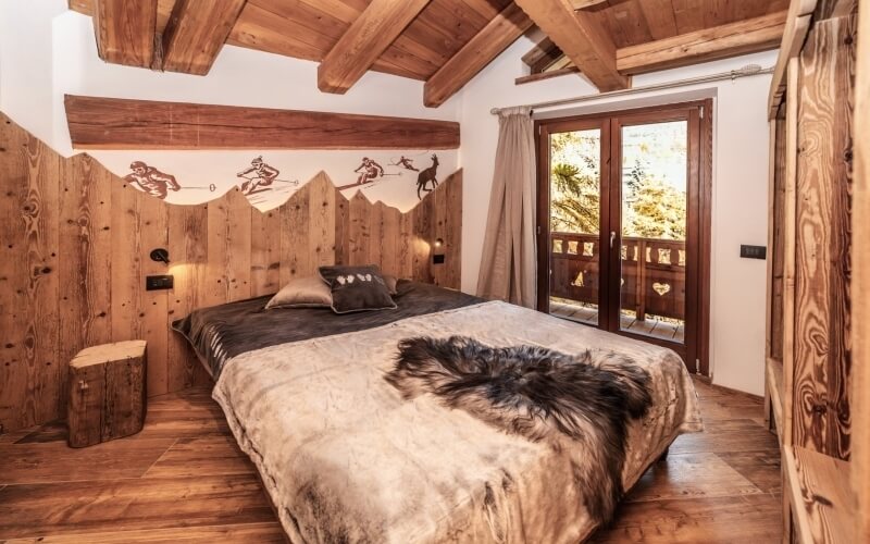 Rustic bedroom with wooden bed frame, mountain mural, large window, and natural materials creating a cozy atmosphere.