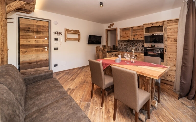 Cozy living room and kitchen with a brown couch, wooden table, white walls, light wood floor, and rustic decorations.