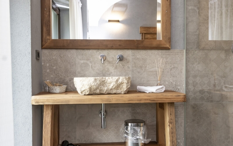 Modern bathroom featuring a light wood vanity, white stone sink, mirror, and beige-tiled walls.