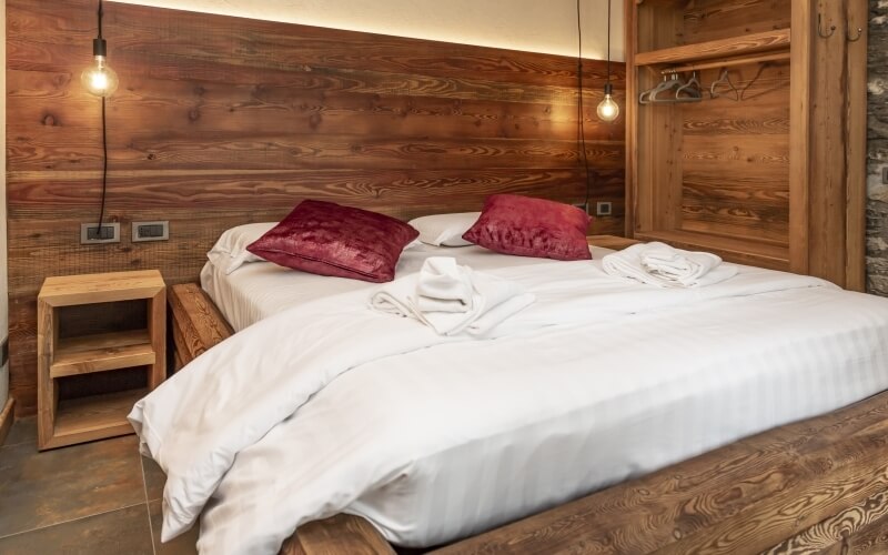 Rustic bedroom with a double bed, nightstand, wooden walls and floor, and two hanging light bulbs.