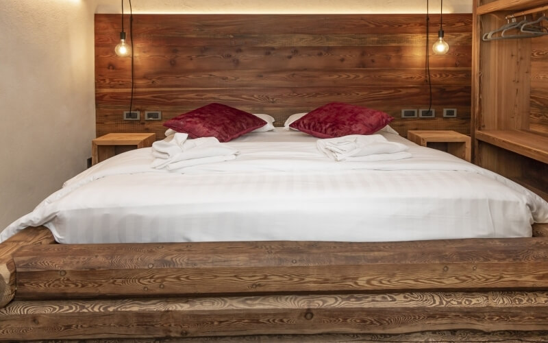 Serene bedroom with a large bed, white sheets, red pillows, wooden wall, soft lighting, and cozy storage options.