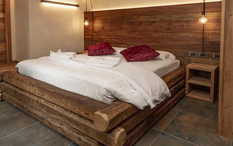 Modern bedroom with a log-framed bed, white and red pillows, warm lighting, and cozy decor in a relaxing atmosphere.