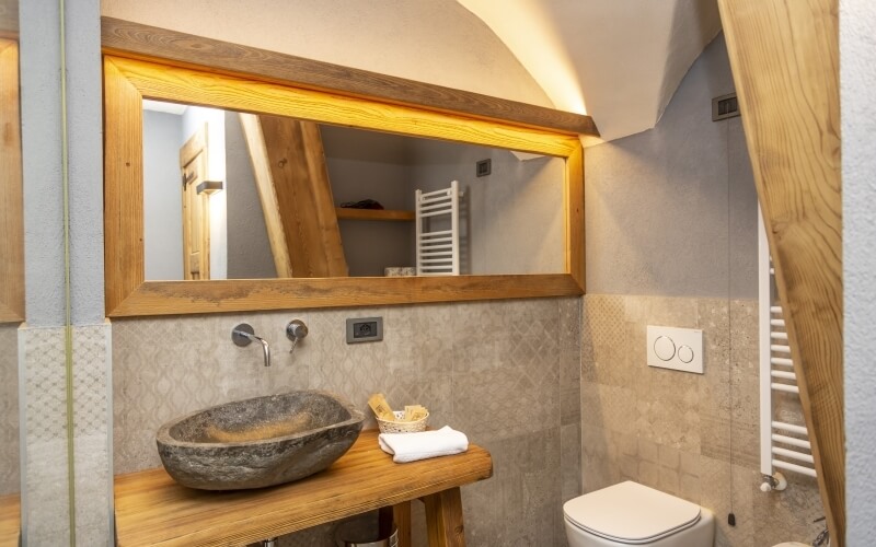 A clean bathroom featuring a wooden vanity, stone sink, large mirror, beige tile walls, and a white toilet.