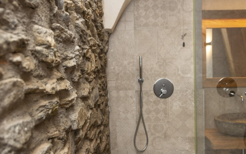 Bathroom with a glass-partitioned shower, stone sink on wood countertop, and a sloped wooden ceiling reflected in the mirror.