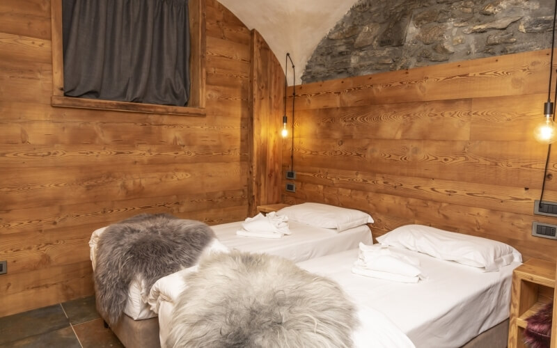 Cozy bedroom with two beds, wooden walls, stone accent, and warm lighting from hanging fixtures.