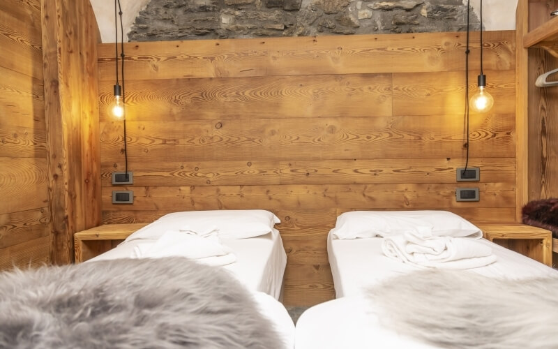 Cozy room with two beds, wooden wall, pendant lights, and a stone wall, creating a warm and inviting atmosphere.