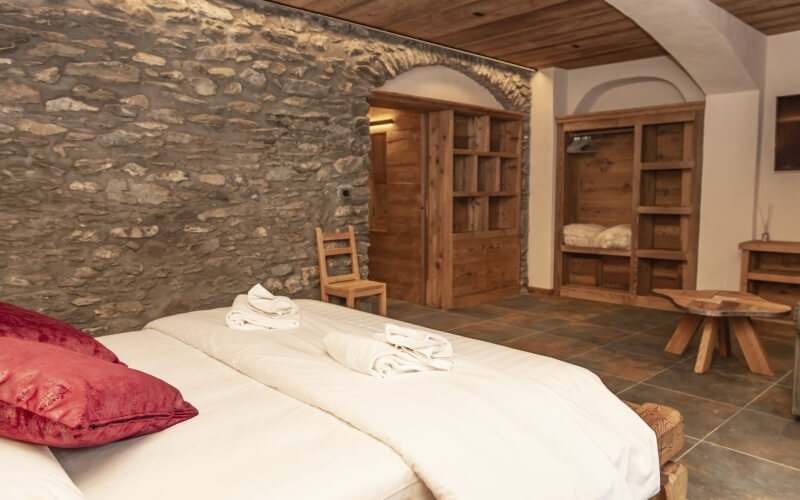 Cozy bedroom with stone walls, two beds with white comforters, wooden furniture, and warm lighting.