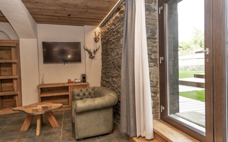 Cozy living room with a stone wall, leather armchair, wooden coffee table, and natural light from a window.