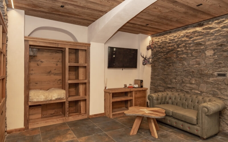 Cozy room with stone wall, wooden ceiling, tan leather sofa, unique table, deer antlers, and warm lighting.