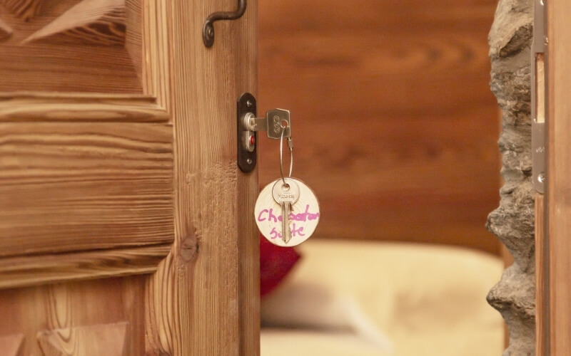 Wooden door with a key in the lock and a tag reading "Chez Henri Suite," blurred room background.