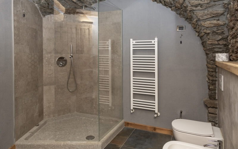 Bagno moderno con doccia in cemento, mosaico decorativo, radiatore bianco e pavimento in piastrelle grigio-nerastre.