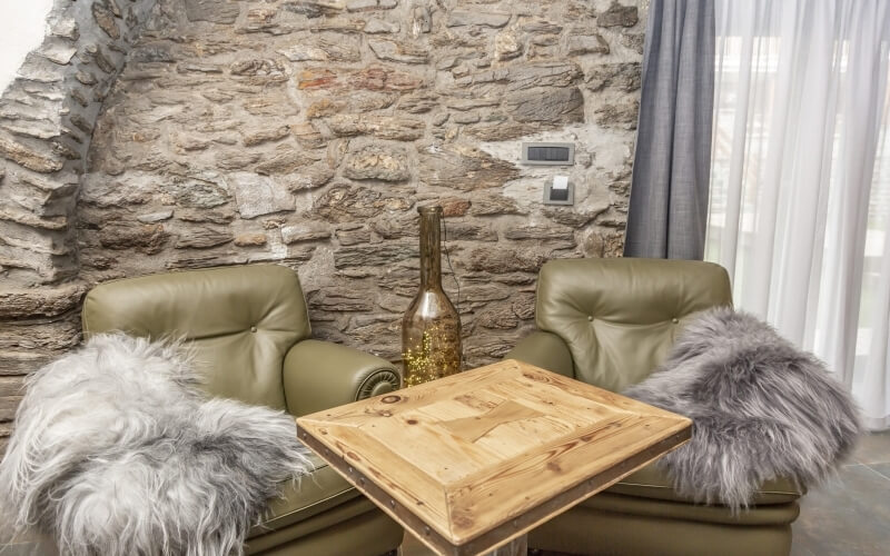 Area di sosta accogliente con poltrone verdi, tavolo in legno, muro di pietra e decorazioni calde e invitanti.