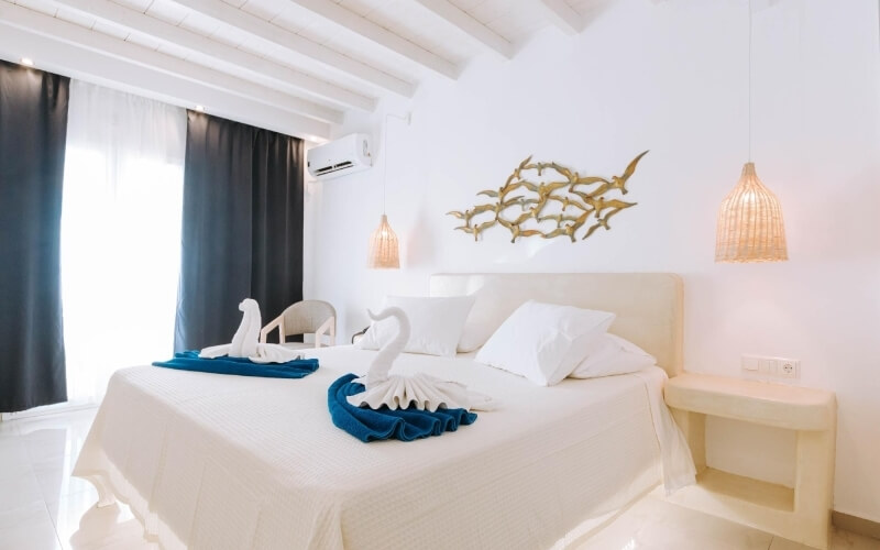 Camera elegante e serena, con letto bianco, asciugamani piegati a forma di cigno e arte murale dorata.