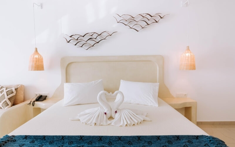 Camera da letto serena con letto bianco, arte di asciugamani a forma di cigni e decorazioni a parete minimaliste.