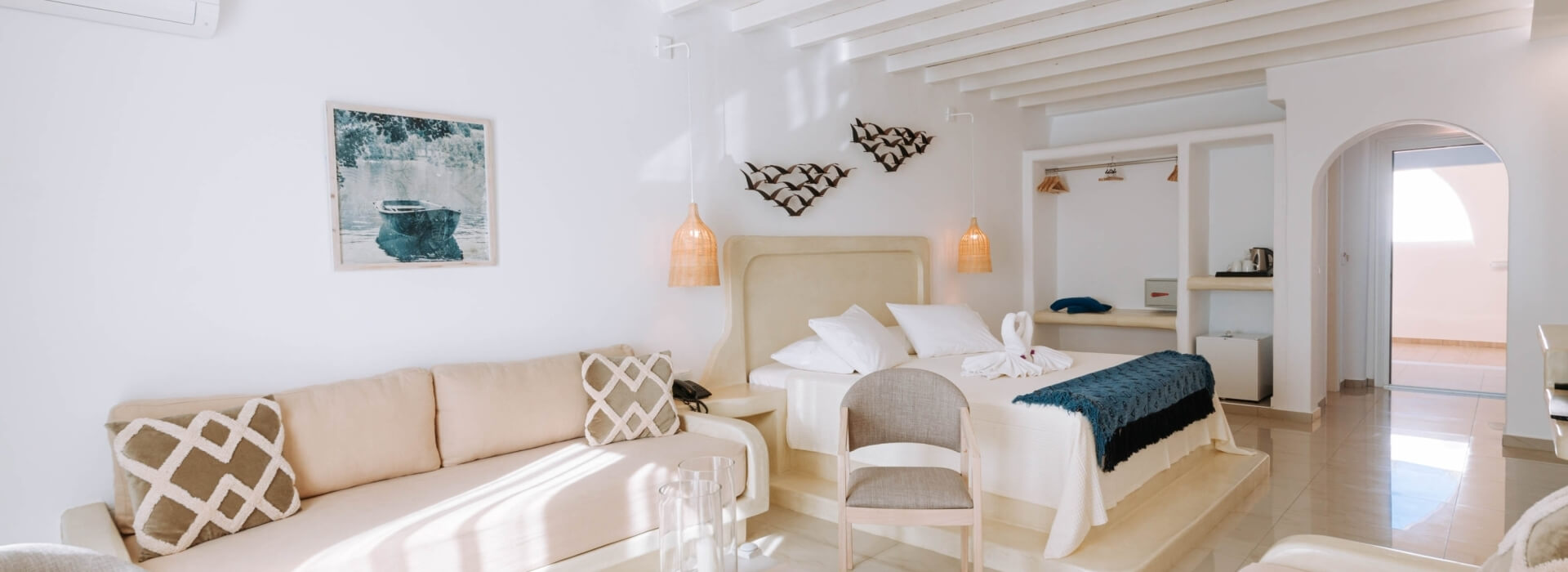 Una stanza serena con un letto bianco, divano, sedia, pareti bianche e luci a sospensione, che invita al relax.