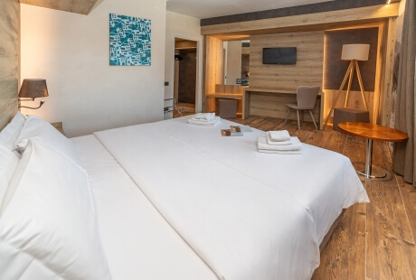 Serene hotel room with white and wood decor, a bed, workspace, abstract painting, and partial bathroom view.