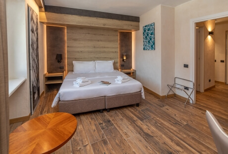 Hotel room featuring a large bed, wooden furniture, lamps, a luggage rack, and a painting on white walls.