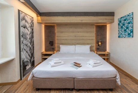 Serene hotel room with a large bed, white linens, artwork, and warm lighting from lamps on nightstands.