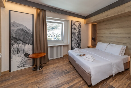 Serene hotel room with a large bed, wooden table, soothing beige walls, and mountain photographs, creating a calming atmosphere.