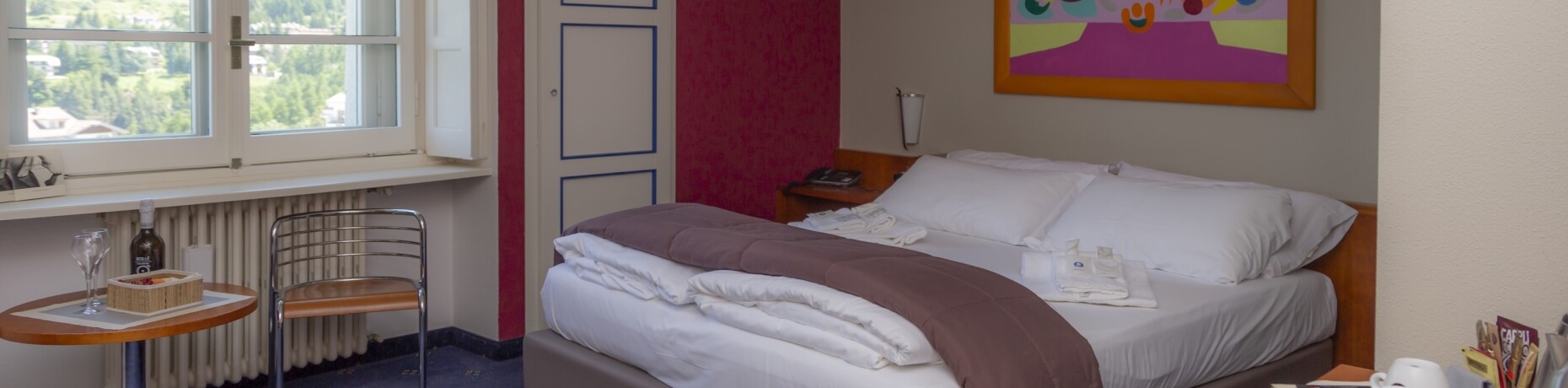 Camera d'hotel accogliente con due letti, tavolo con vino, finestra con vista e vari comfort per gli ospiti.