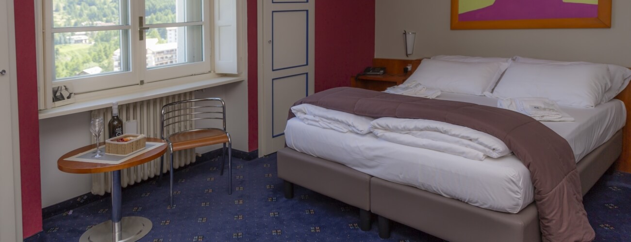Cozy hotel room featuring a bed, round table with food, modern chair, and a large window with a green landscape view.