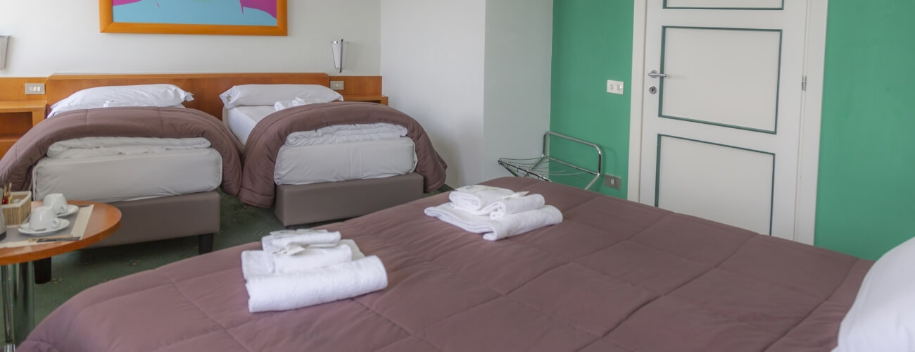 Hotel room with two neatly made beds, towels, linens, and a small table with dining items, suggesting comfort and readiness.