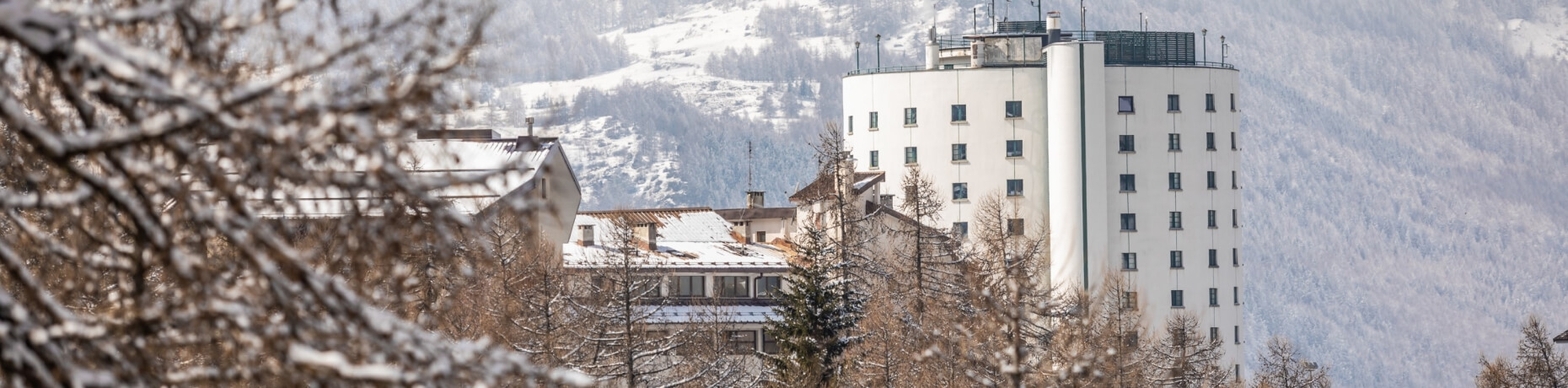 Scena invernale serena con un grande edificio bianco circondato da alberi innevati e colline ondulate sullo sfondo.