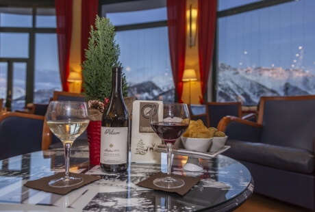 Table with wine glasses and snacks, snowy mountains in the background, creating a cozy winter evening atmosphere.