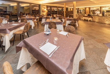 Spacious dining area with brown tablecloths, leather chairs, and a chef in the background, creating a warm, inviting atmosphere.