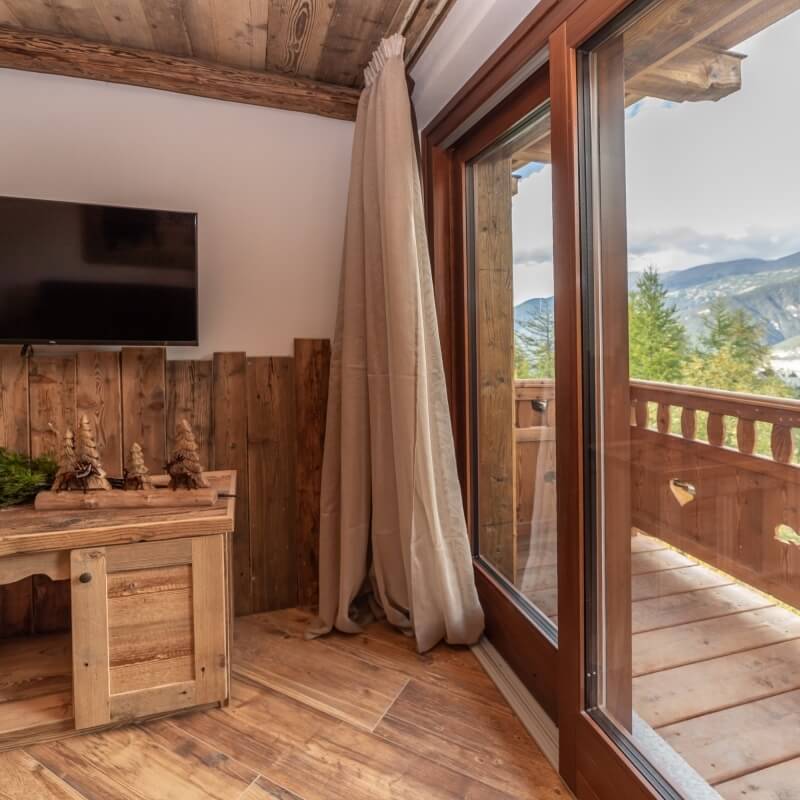 Cozy rustic room with a sliding glass door to a wooden balcony, showcasing a scenic view of mountains and trees.