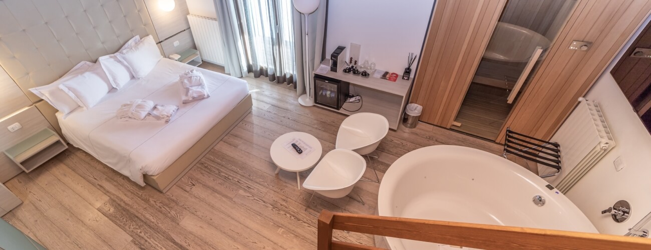 Camera d'albergo con letto grande, vasca, tavoli circolari e frigorifero, arredamento pulito e accogliente.