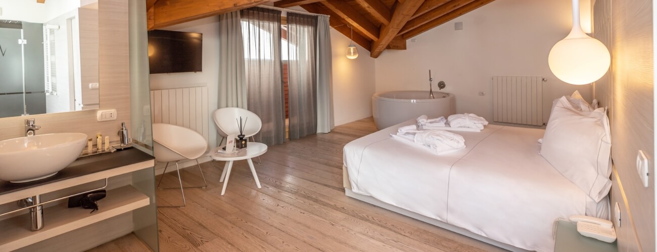 Camera d'albergo serena con letto king, bagno moderno e decorazioni bianche e legno chiaro, illuminata da luce naturale.