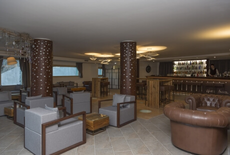 Spacious lounge with gray chairs, brown leather couch, bar area, and inviting ambiance, featuring mixed furniture styles.