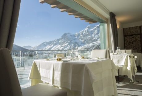 Luxurious dining room with tables set for guests, large window showcasing snow-capped mountains in the background.