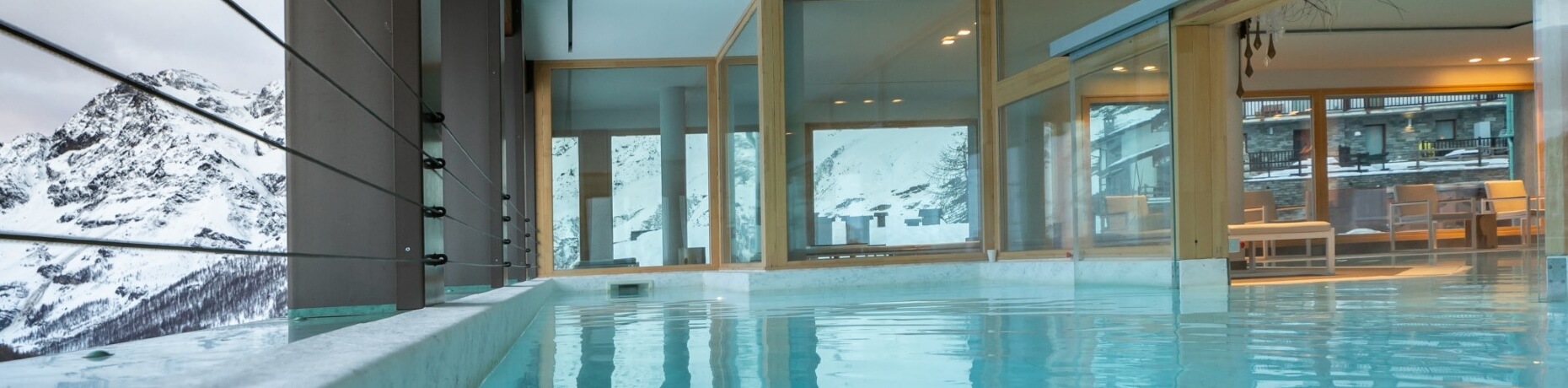 Indoor pool with glass wall, marble ledge, and mountain view, creating a serene and tranquil atmosphere.