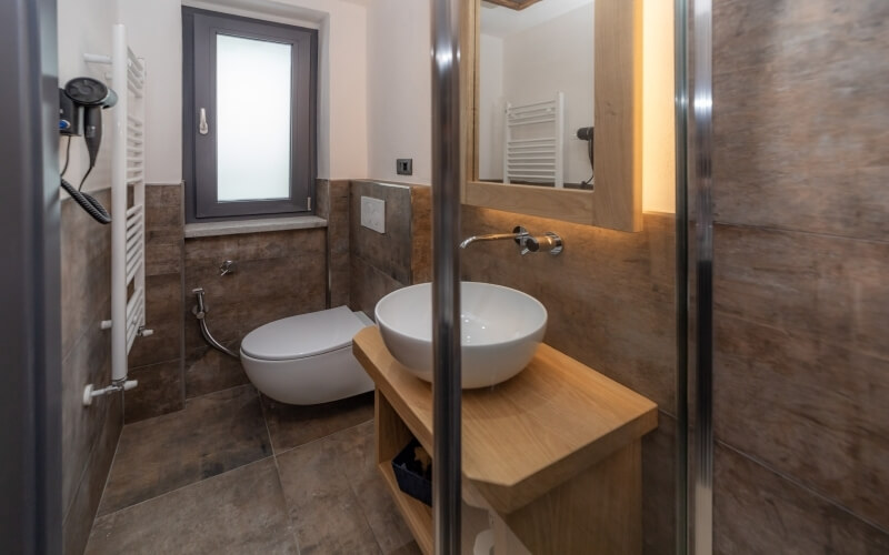 Modern bathroom with brown tiles, white toilet, sink on wooden vanity, mirror, and radiator with hair dryer. Clean and minimalist.