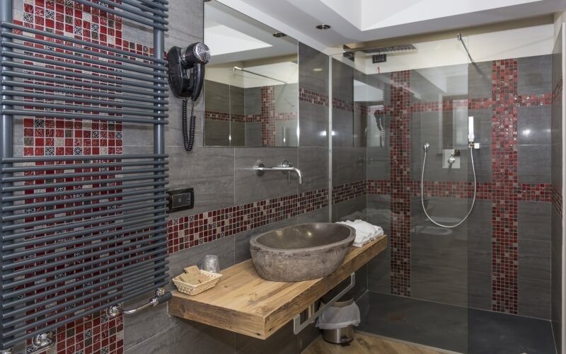 A modern bathroom featuring a gray sink, towel rack, glass shower, and red accents, with wooden flooring and toiletries.