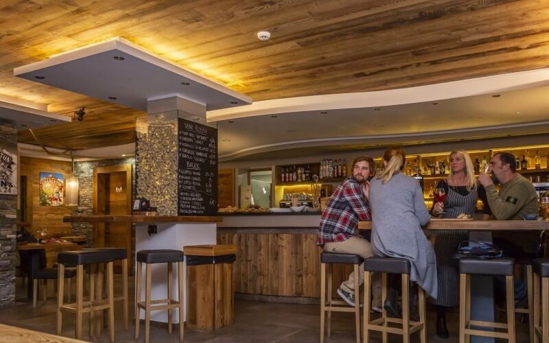 Contemporary bar scene with three patrons at a wooden bar, drinks in hand, and a blackboard menu in a cozy atmosphere.