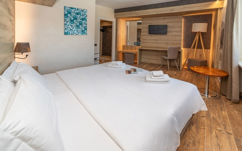 Camera d'hotel pulita con letto grande, scrivania, TV, tavolo rotondo e dipinto astratto blu e bianco.