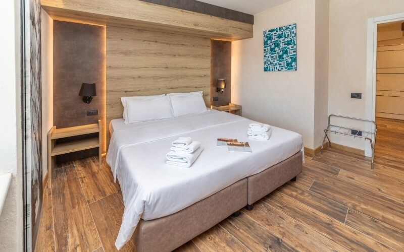 Serene hotel room with a spacious bed, white linens, nightstands, black lamps, and a vibrant blue abstract painting.