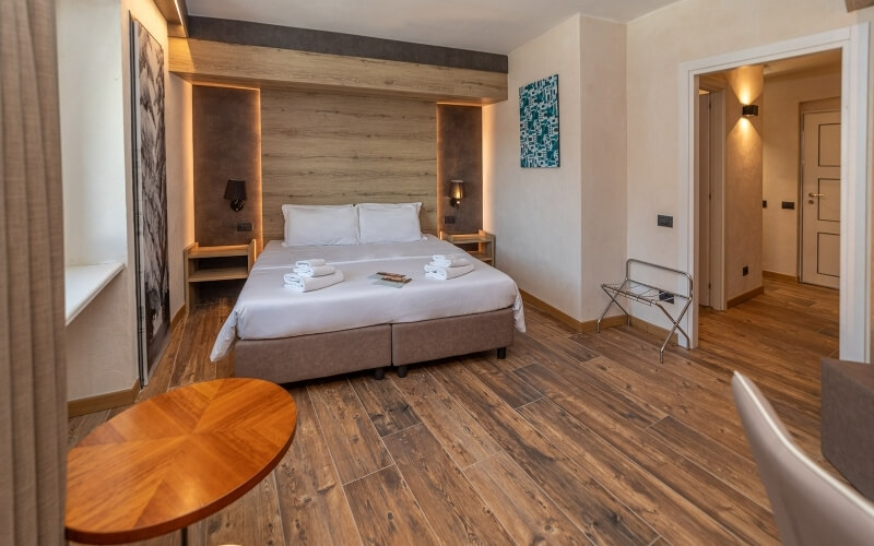 Modern hotel room with a large bed, desk, warm lighting, and inviting decor. White walls and dark hardwood floor.