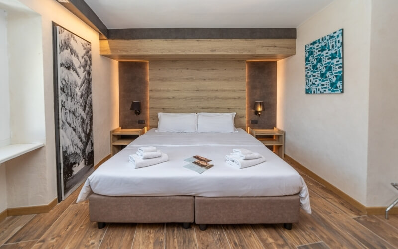 Serene hotel room with a spacious bed, white linens, folded towels, nightstands, and wall-mounted lamps.