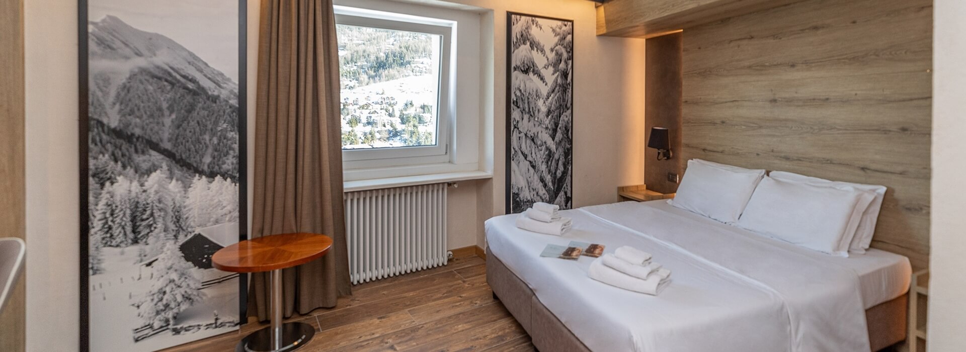 Camera d'albergo minimalista con vista su un paesaggio invernale, letti bianchi e decorazioni in bianco e nero.