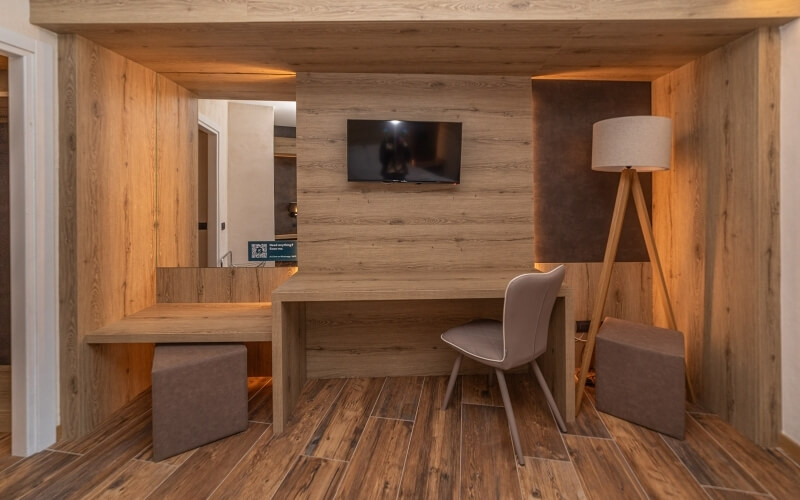 Modern room with wooden desk, gray chair, wall-mounted TV, lamp, and two gray stools under the desk.
