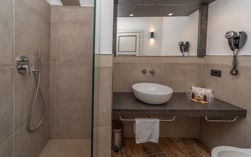 Modern bathroom with a glass shower, white oval sink on a dark countertop, and a large mirror reflecting light.