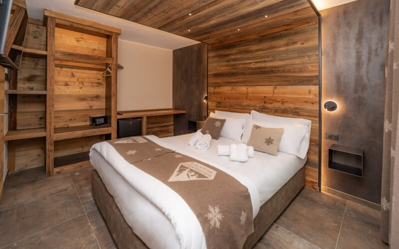 Camera da letto rustica e accogliente con letto grande, lenzuola bianche, decorazioni in legno e illuminazione soffusa.