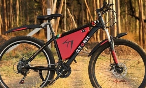 Black and red electric mountain bike in a forest, showcasing "STORM" branding, with a torpedo-shaped battery and off-road tires.