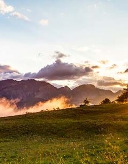 Serene landscape with misty mountains, lush green field, and a blue-white sky, evoking tranquility and natural beauty.