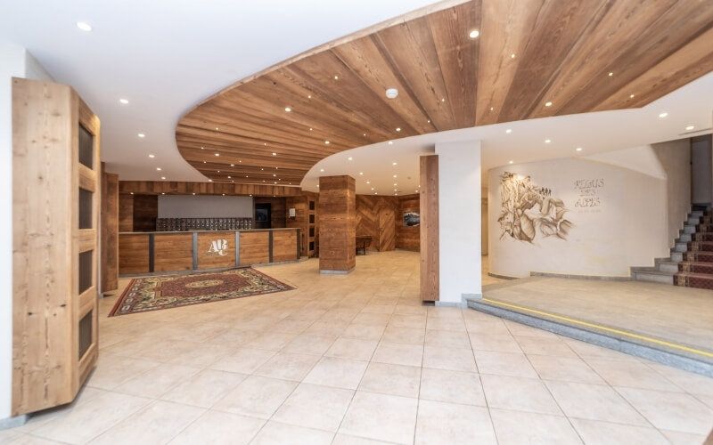Spacious, well-lit room with wooden paneling, high ceiling, area rug, and a distant bar area, suggesting a hotel lobby.